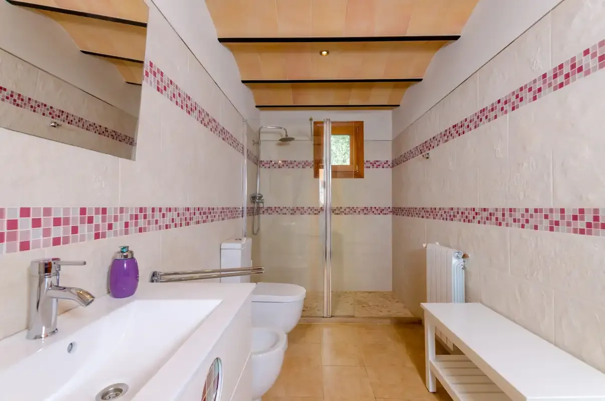 A tiled bathroom with a sink, shower, toilet, and window.