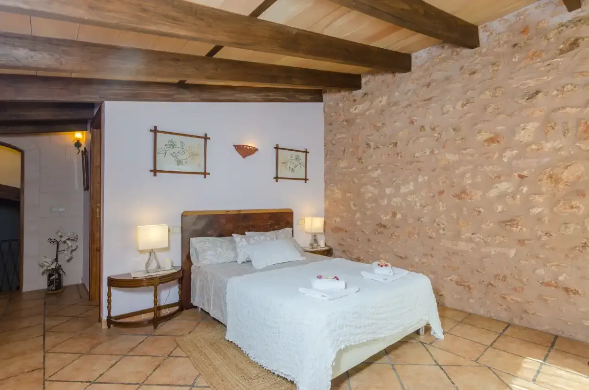 A bedroom with a bed, bedside tables, and exposed wooden ceiling beams.