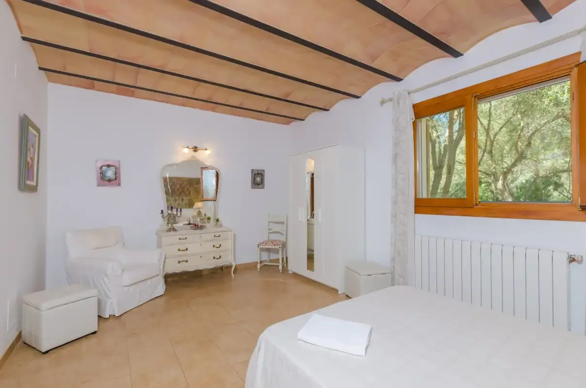 A bright bedroom with a bed, seating, and a large window overlooking trees.
