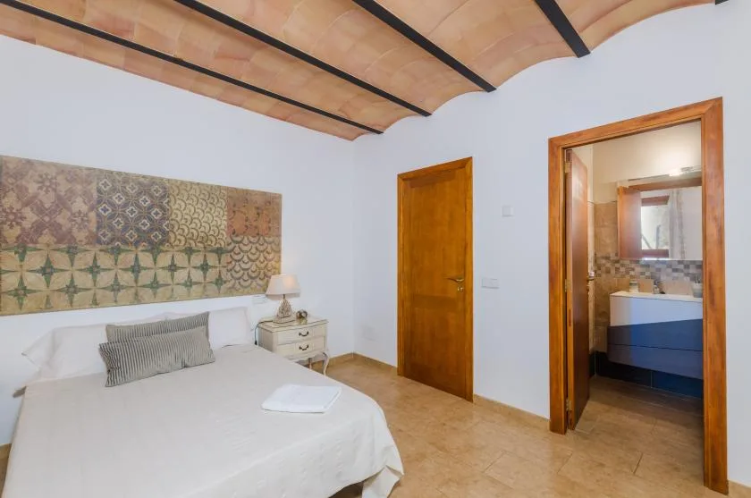 A bedroom with a bed beneath patterned wall tiles and a wooden ceiling.
