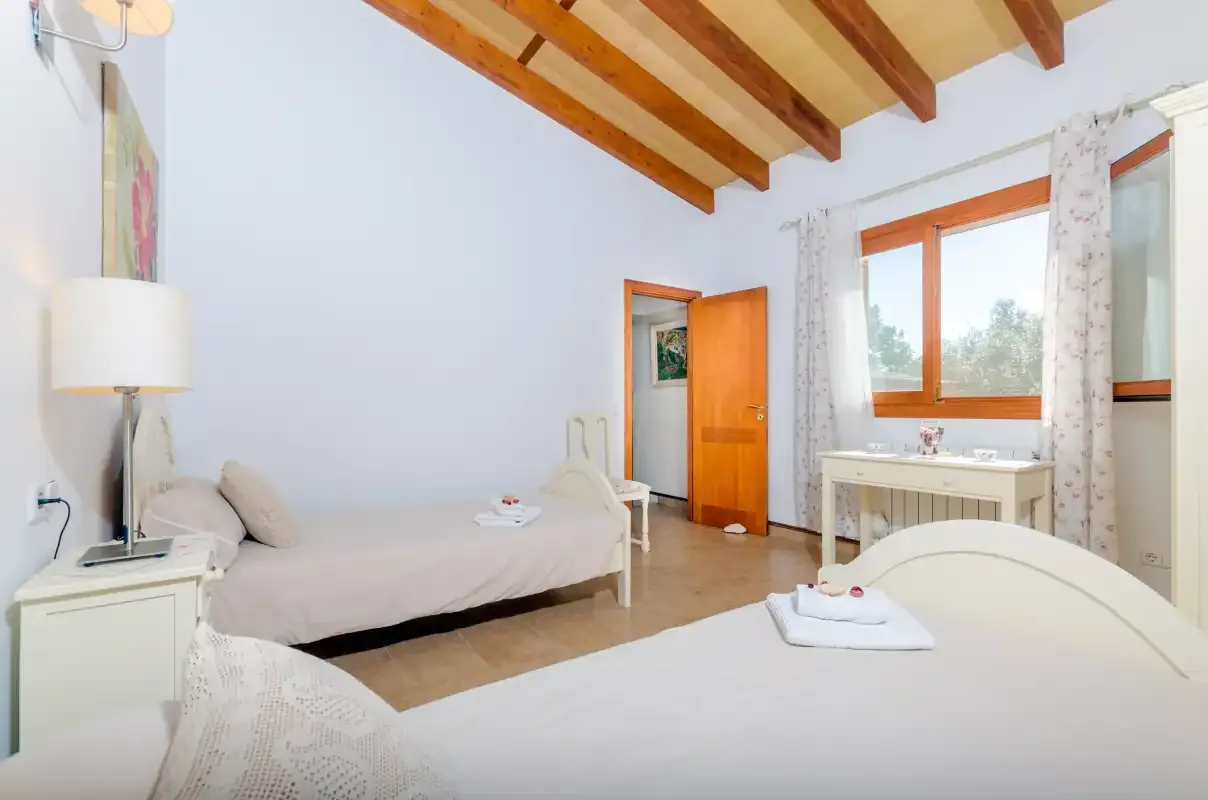 A bright bedroom with two beds, exposed ceiling beams, and a wooden door.