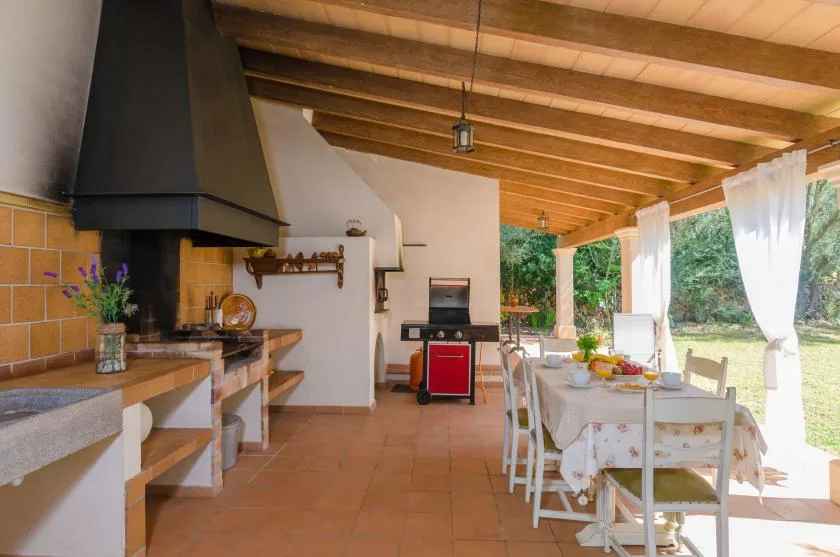 An open kitchen and dining area with a long table beside a curtained outdoor view.