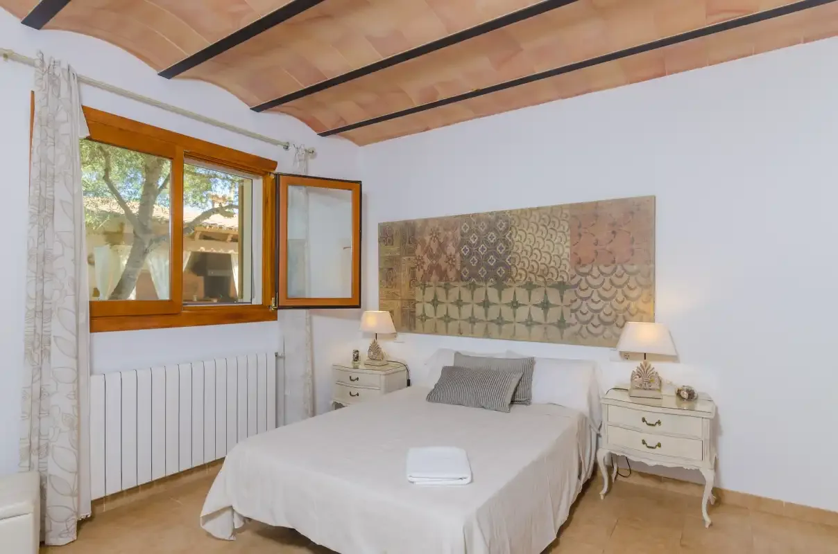 A bedroom with a double bed, bedside tables, and a window.