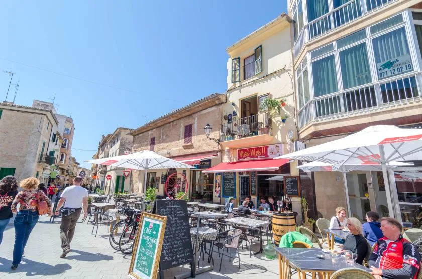 A sunny street café with outdoor tables and umbrellas along a row of buildings.
