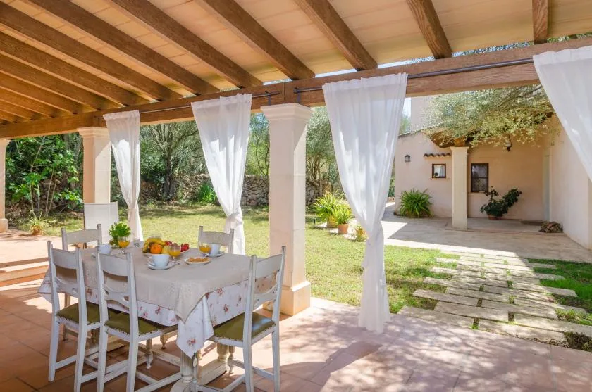A covered patio with a dining table overlooks a garden and a small courtyard.