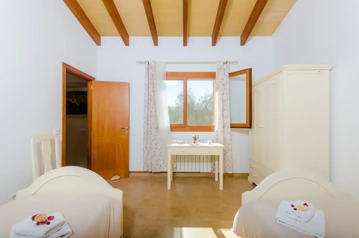 A bright bedroom with two single beds, a window, and a small table.