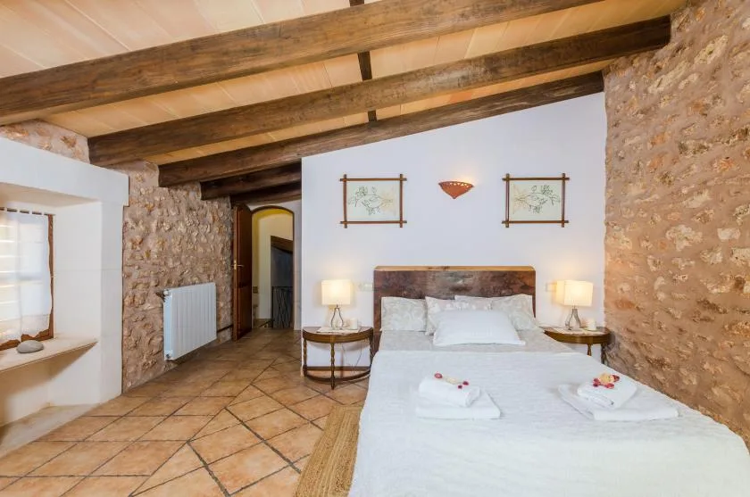 A bedroom with a bed, exposed wooden ceiling beams, and stone walls.