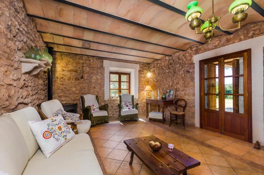 A rustic stone living room with seating, a wooden coffee table, and glazed doors.