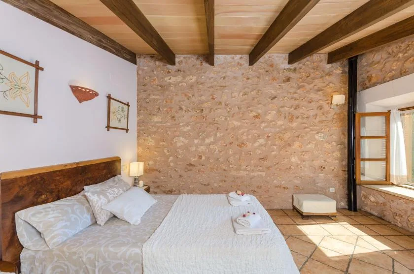 A bedroom with a bed, exposed ceiling beams, and a stone wall.
