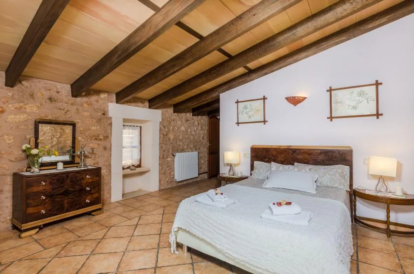 A bedroom with a bed beneath exposed wooden ceiling beams.