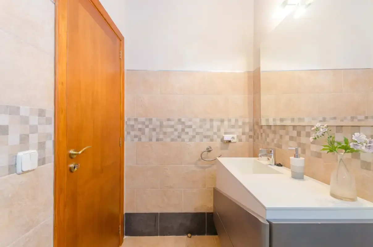 A bathroom with a long vanity and light tiled walls.