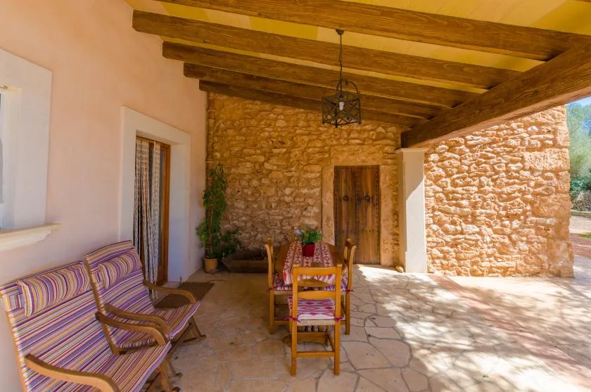 A covered stone patio with striped seating and a wooden dining table.