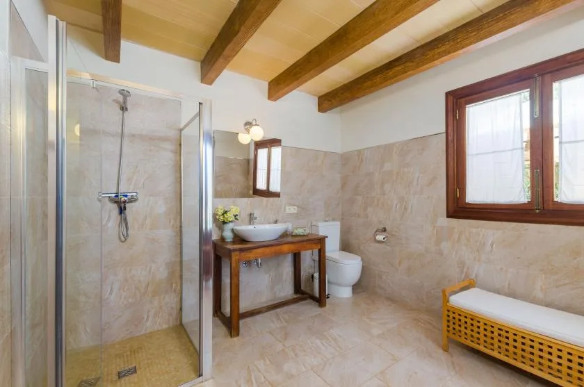 A bathroom with a glass shower, sink, and wooden ceiling beams.