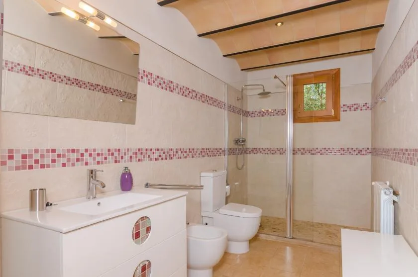 A tiled bathroom with a sink, shower, toilet, and small window.