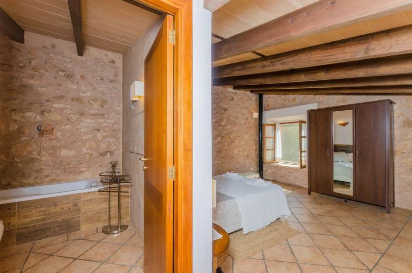 A bedroom with an adjoining bathtub area, exposed beams, and stone walls.