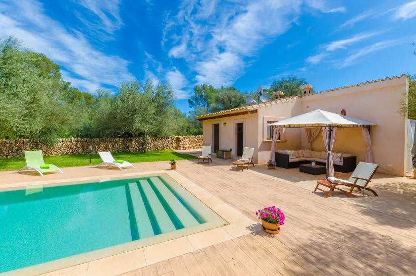 An outdoor swimming pool beside a sunlit patio with lounge seating.