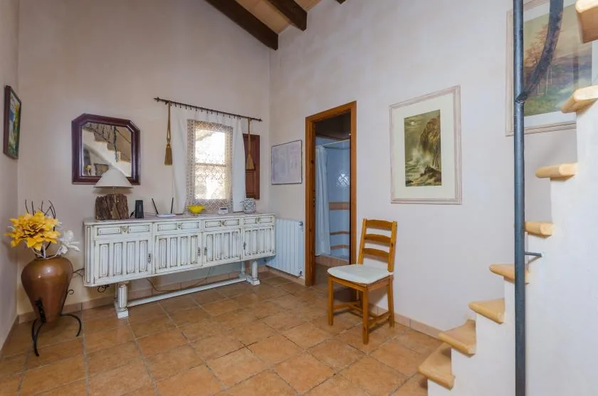 A bright room with a long sideboard, a wooden chair, and a staircase.