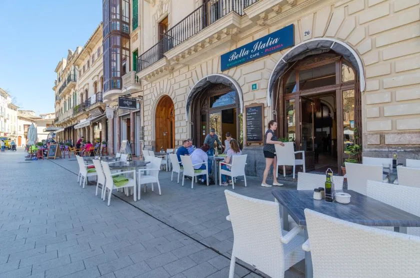 Outdoor café seating lines a paved pedestrian street beside arched storefronts.