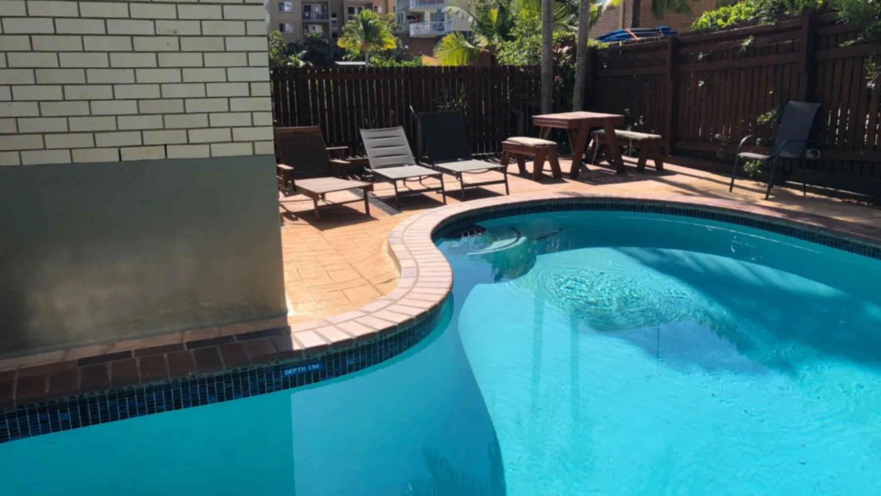 Una piscina al aire libre está junto a un patio pavimentado con asientos.
