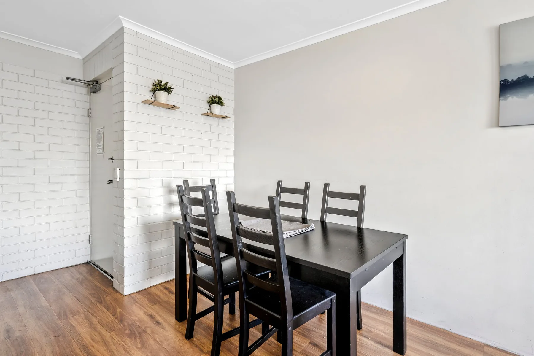 Comedor con una mesa oscura y sillas junto a una pared de ladrillo blanco.
