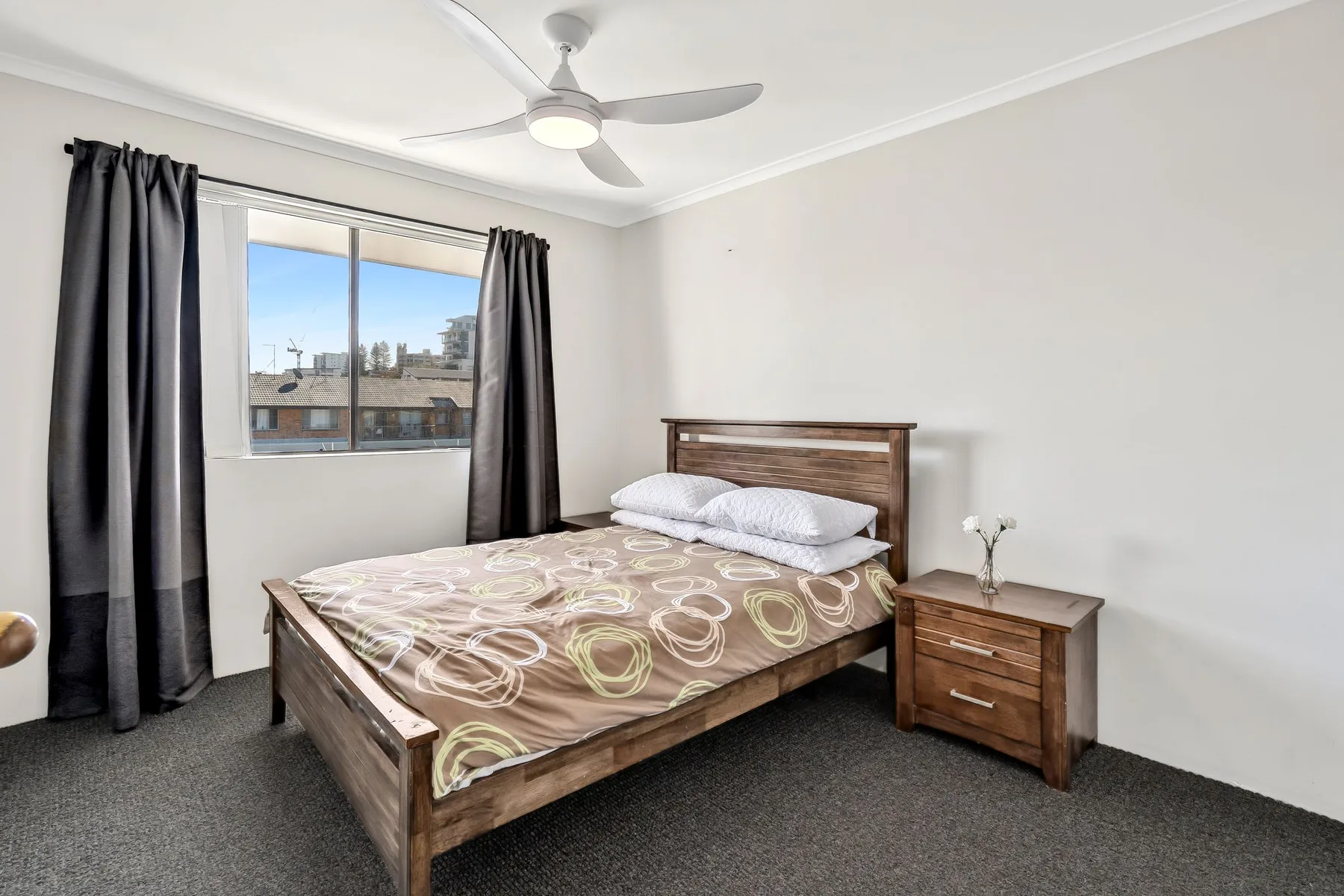 Un dormitorio con una cama de madera, una mesita de noche y una ventana con cortinas.