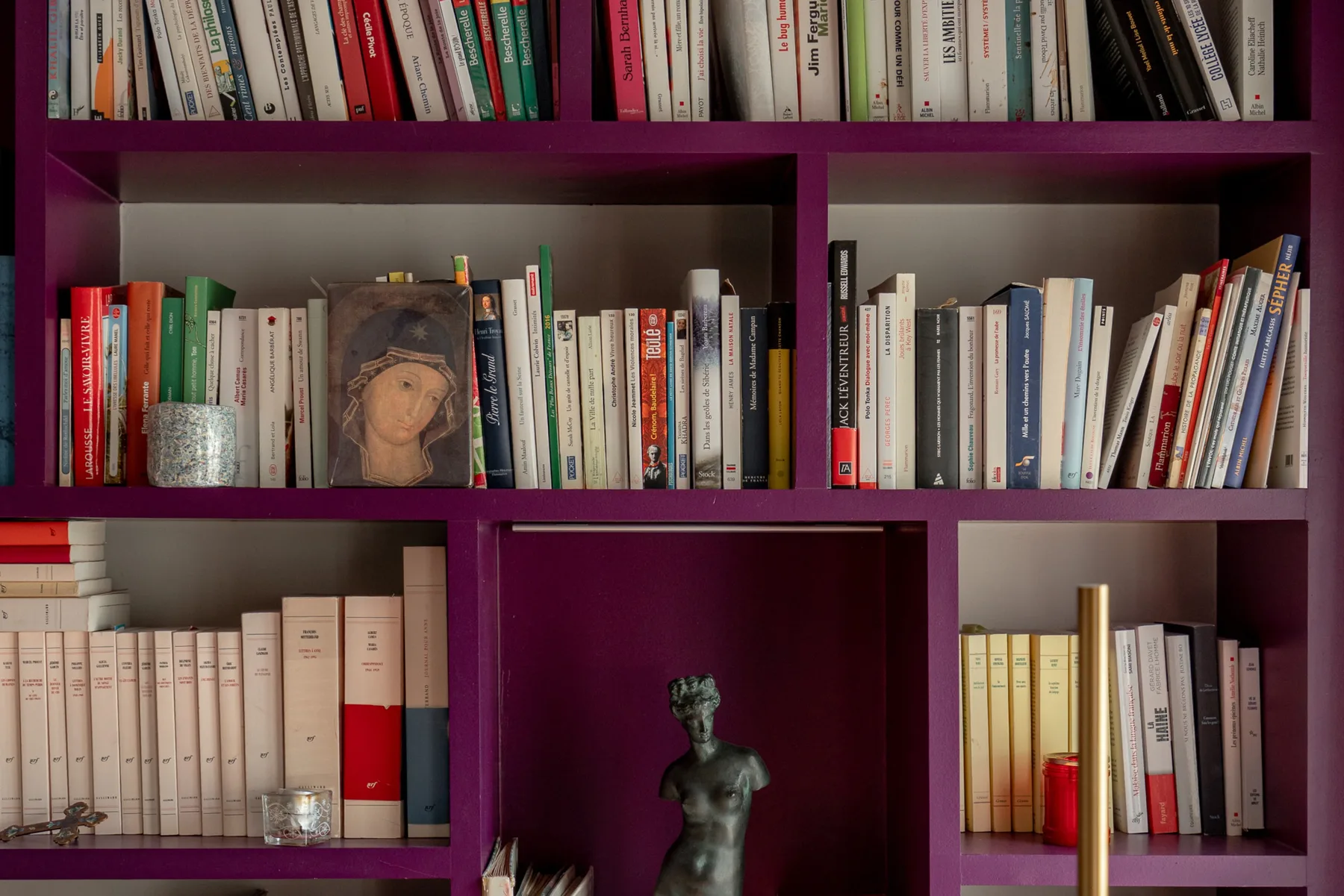 Una estantería morada llena de libros y una pequeña escultura.