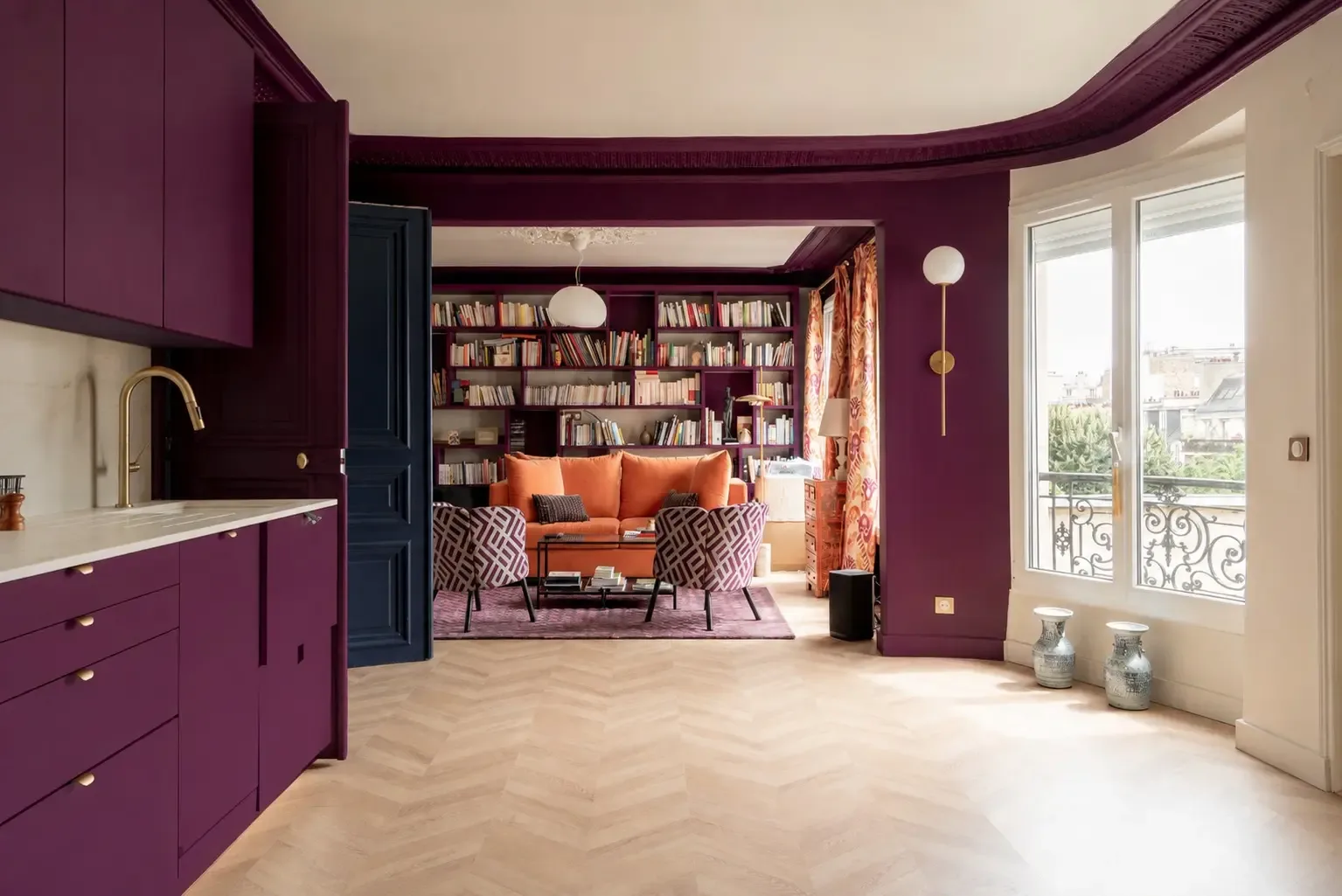 Una sala de estar con estanterías, asientos naranjas y una zona de cocina morada.