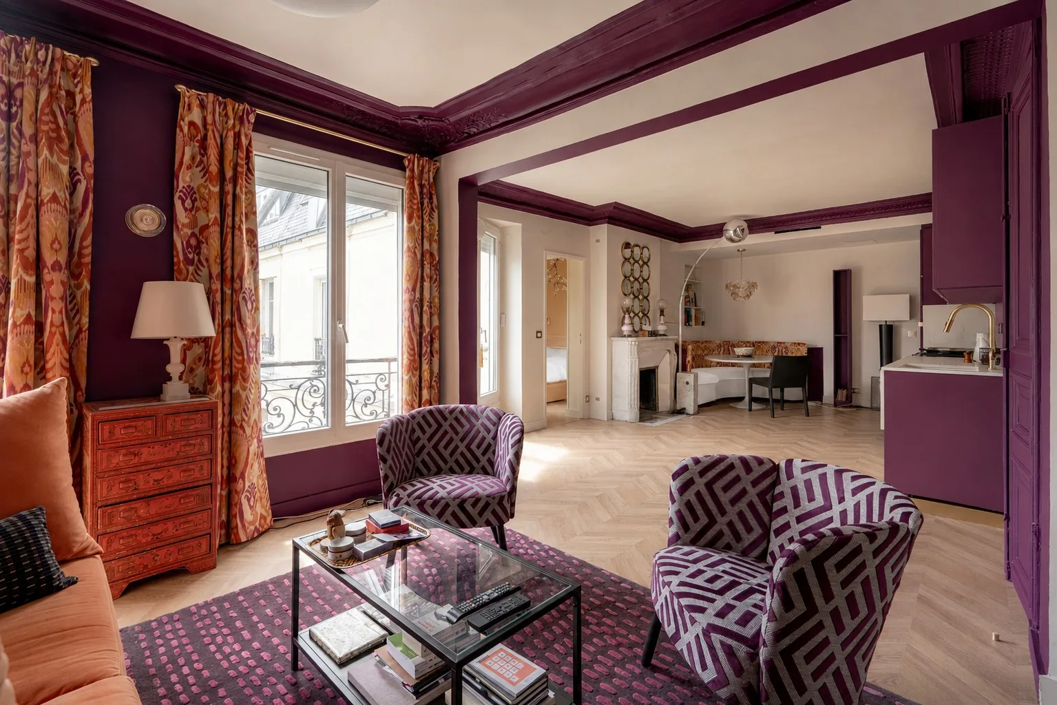 Una sala de estar con asientos estampados y una mesa de centro de vidrio junto a ventanas altas.