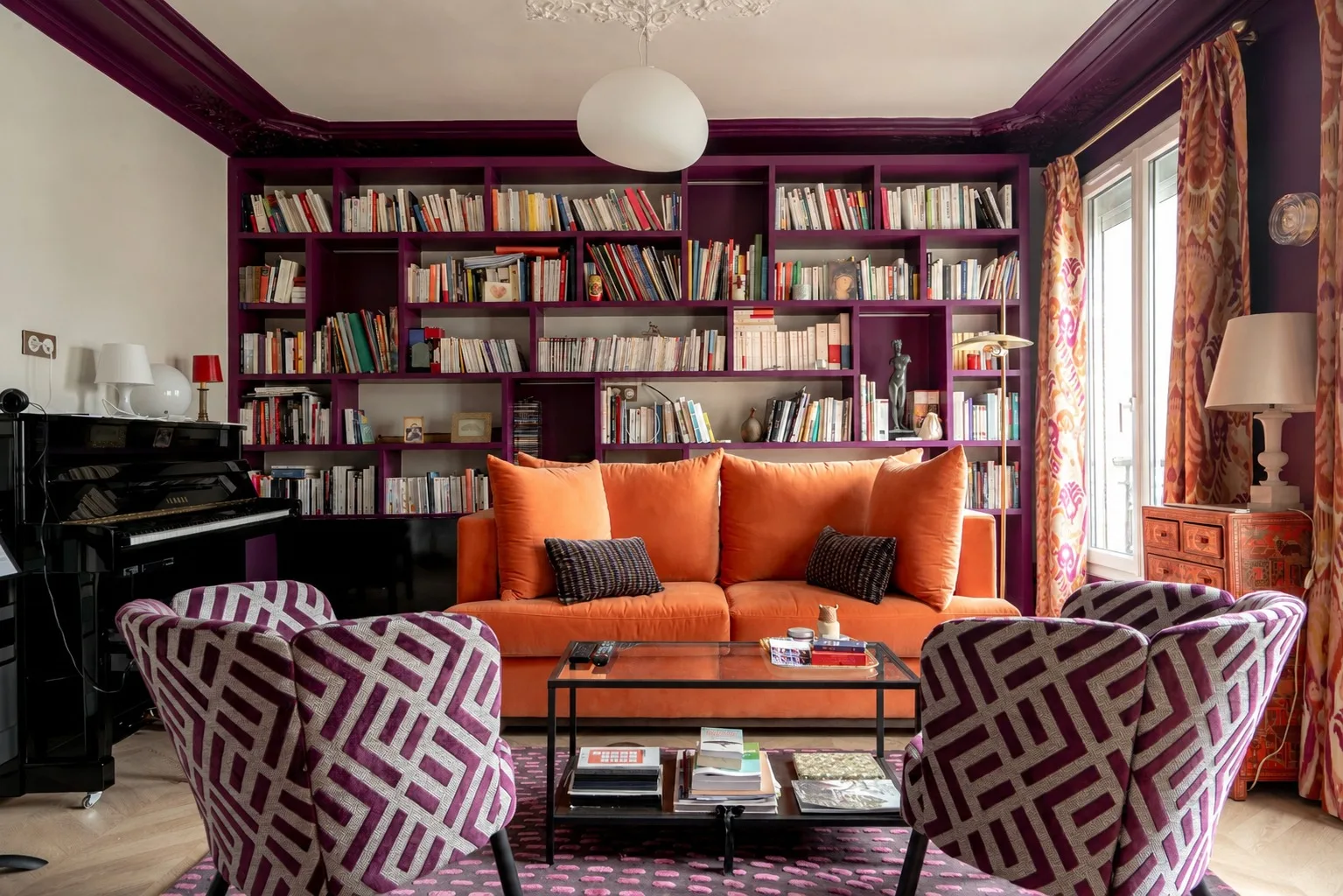 Una sala colorida con asientos naranjas, sillones estampados y estanterías.