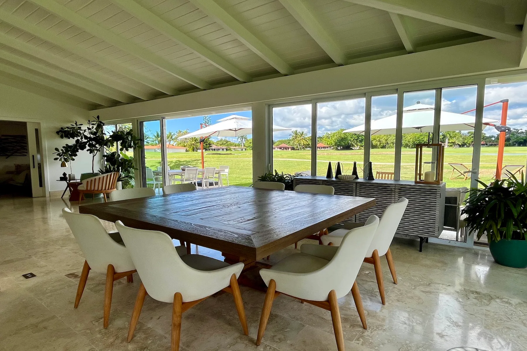 Un comedor con una gran mesa de madera y sillas junto a amplias ventanas con vista al césped.