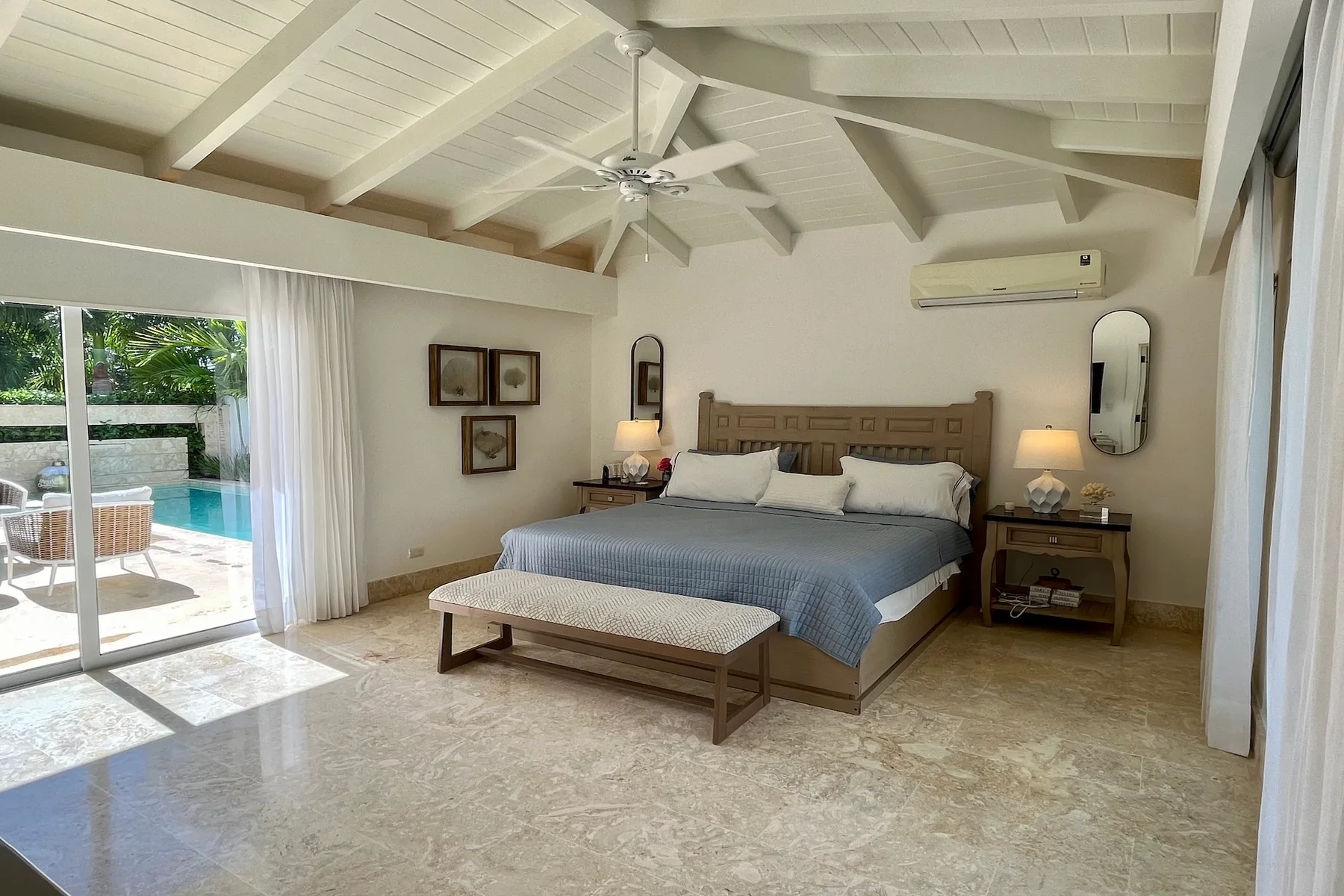 Un dormitorio luminoso con una cama grande y puertas corredizas de vidrio que dan a un patio junto a la piscina.