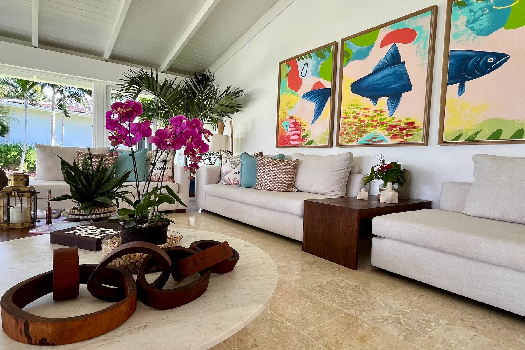 Una sala luminosa con asientos blancos, plantas tropicales y coloridas pinturas de peces.
