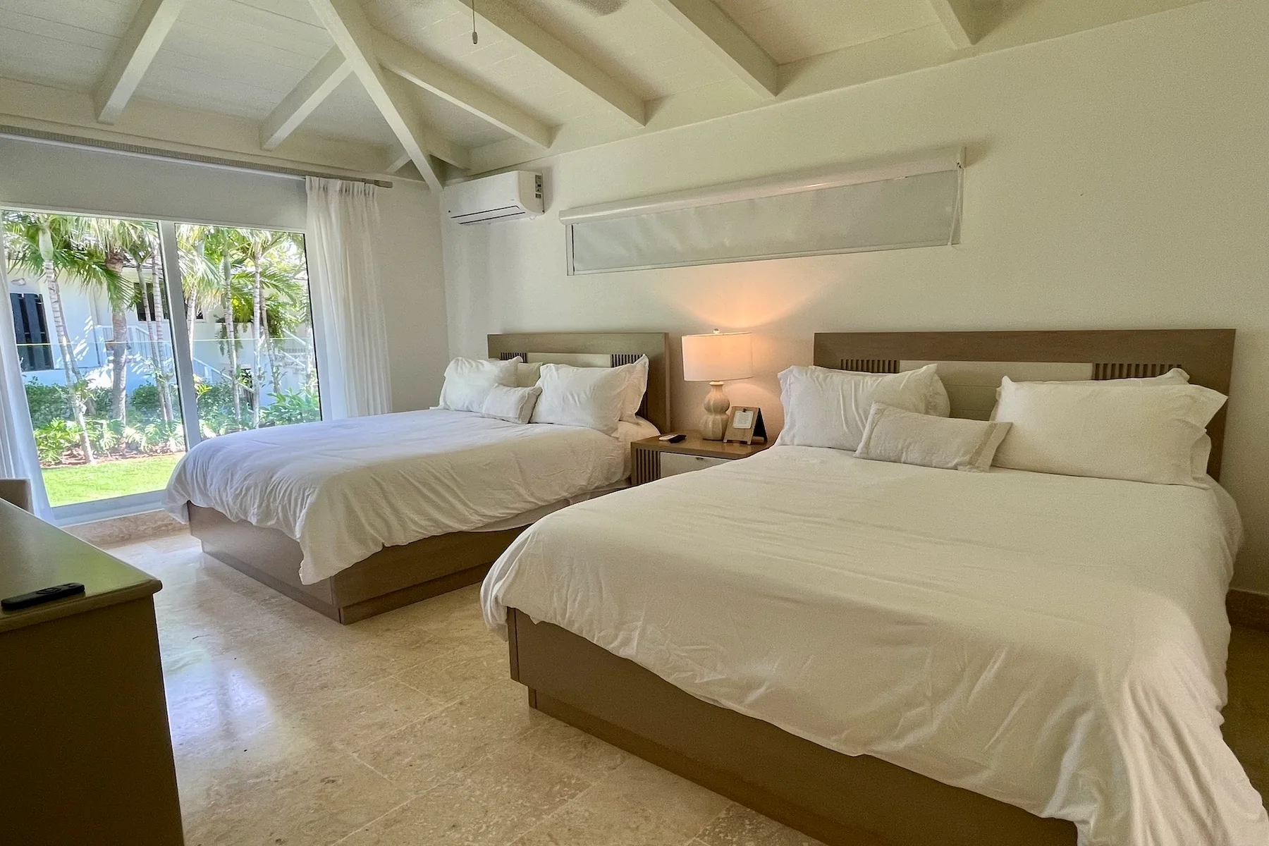Un dormitorio luminoso con dos camas, ropa de cama blanca y una ventana grande.