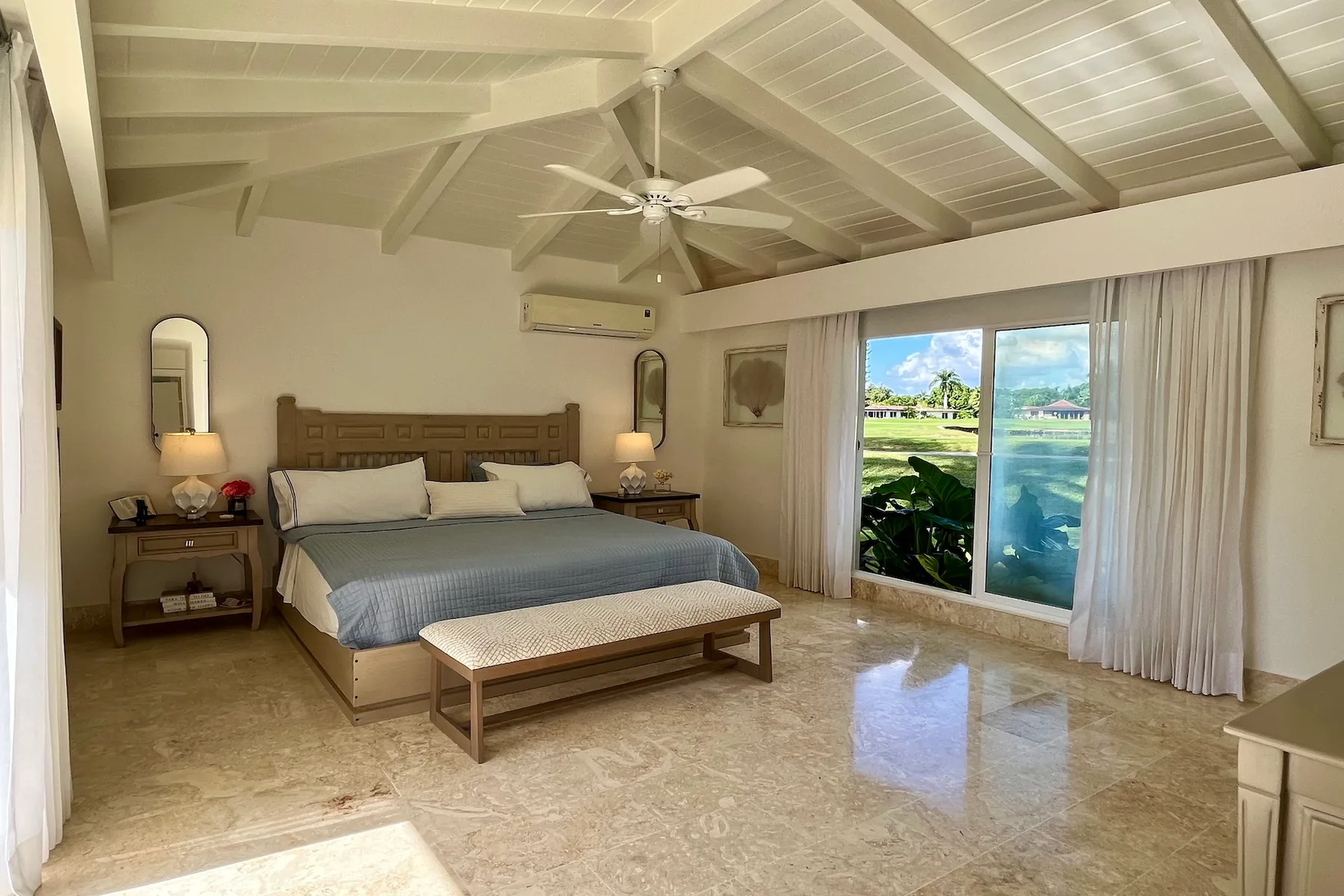 Dormitorio con una cama y una puerta corrediza de vidrio con vistas a un jardín y al agua.