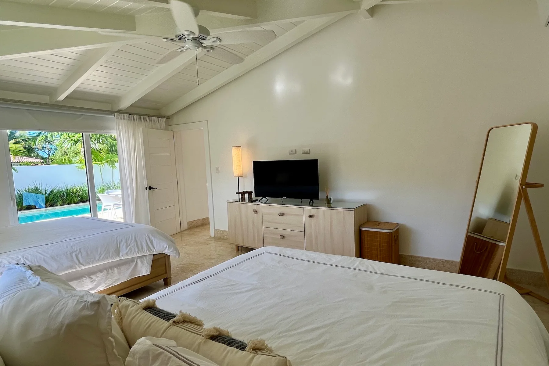 Dormitorio luminoso con dos camas, un televisor y vistas a la piscina.