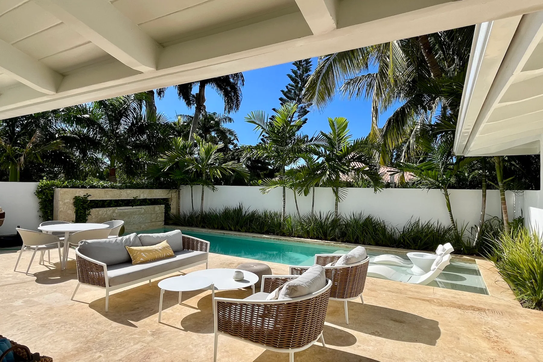 Un patio junto a una piscina al aire libre, con asientos y plantas tropicales.