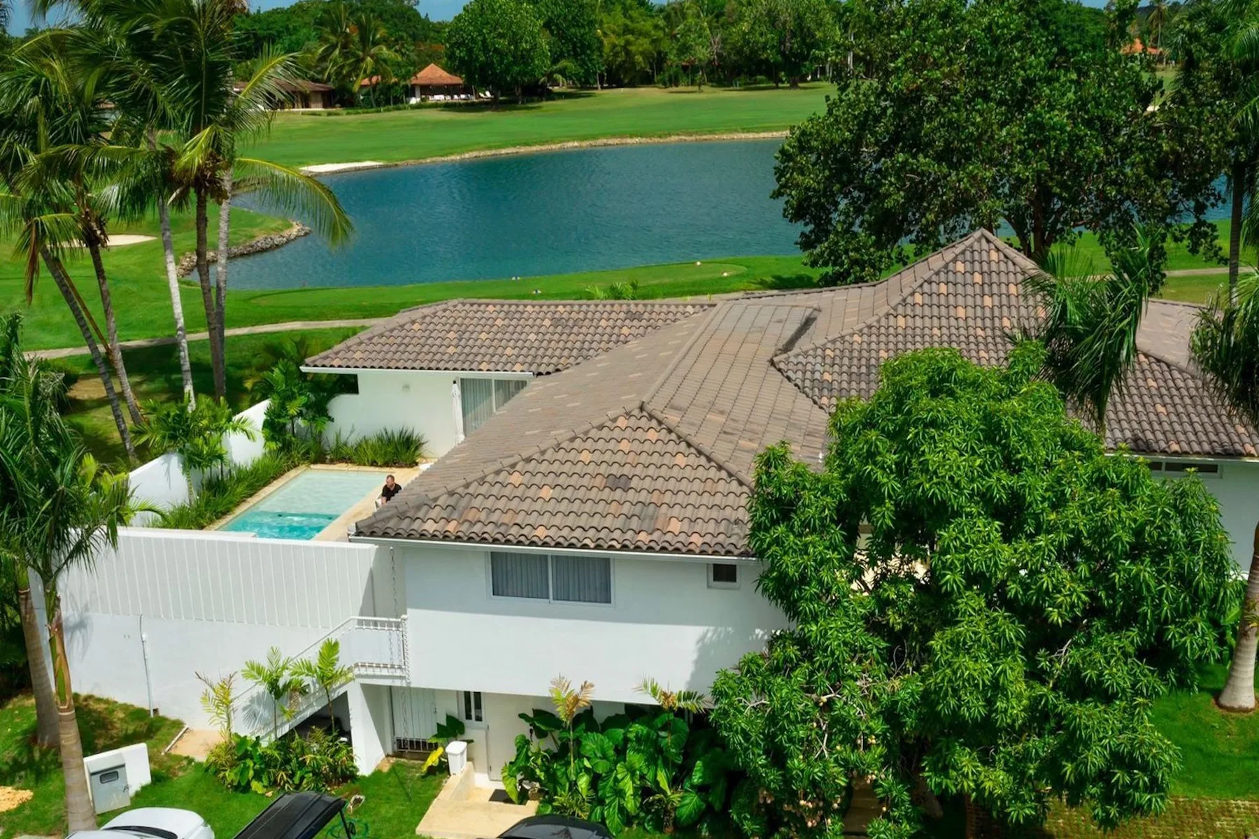 Una casa blanca con techo de tejas está junto a un césped verde y un lago.
