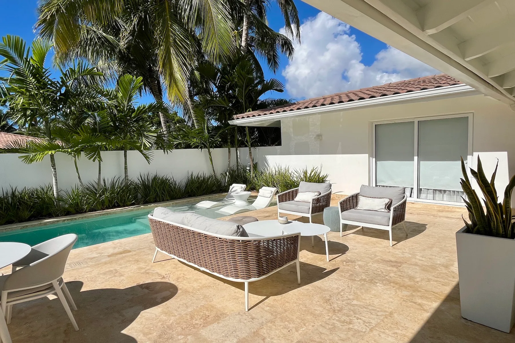 Un patio exterior con asientos junto a una piscina y puertas corredizas de vidrio.