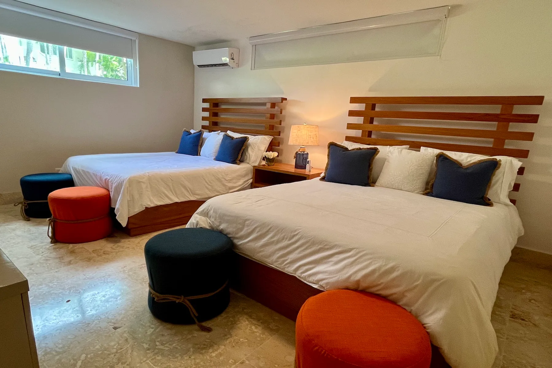 Un dormitorio con dos camas, mesitas de noche y taburetes redondos de colores.