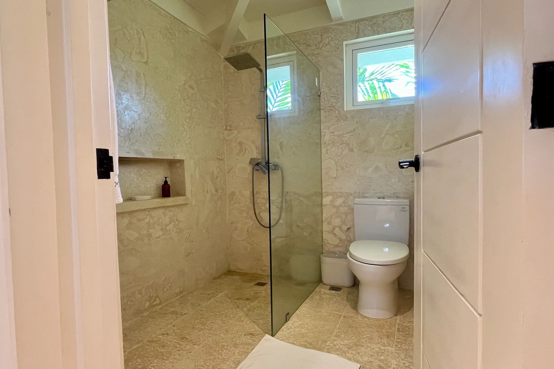 Un baño con ducha de vidrio, inodoro y dos ventanas pequeñas.