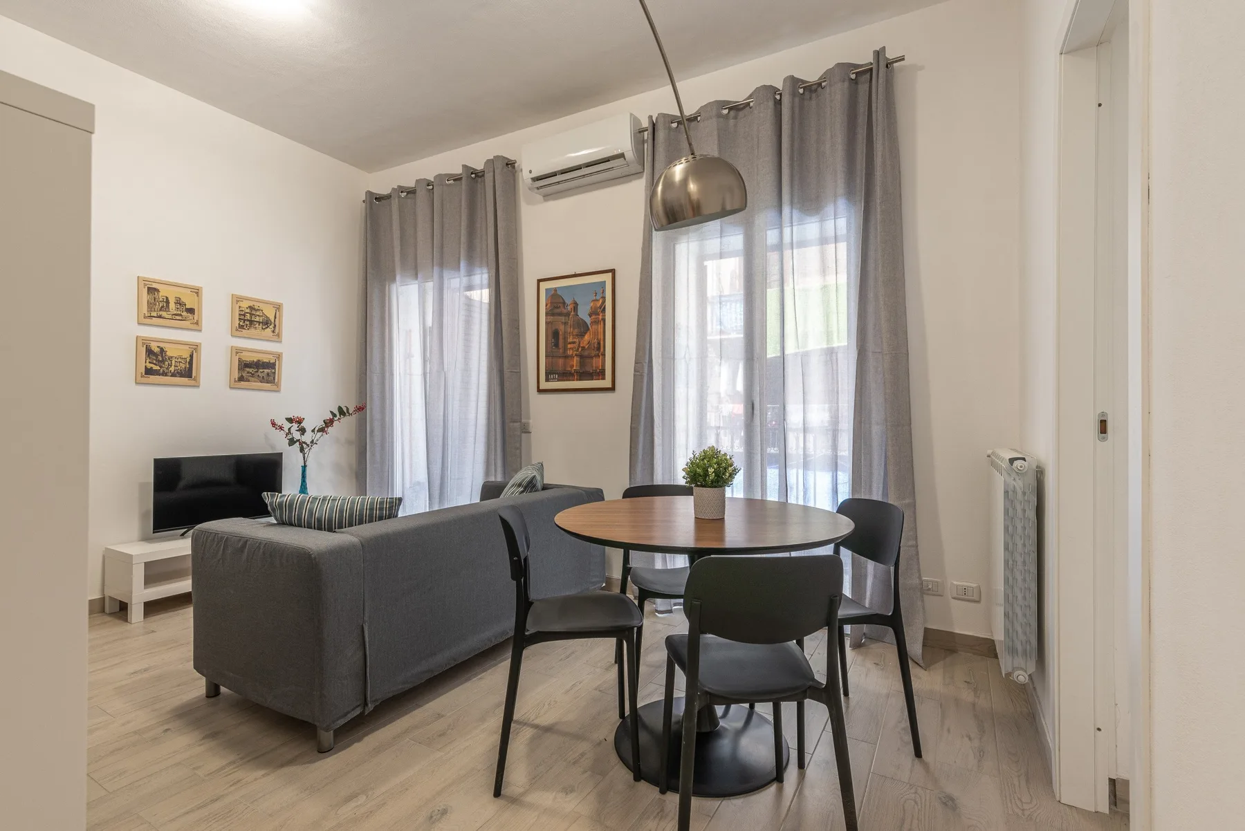 Una sala de estar y comedor con asientos, una mesa redonda y ventanas altas.