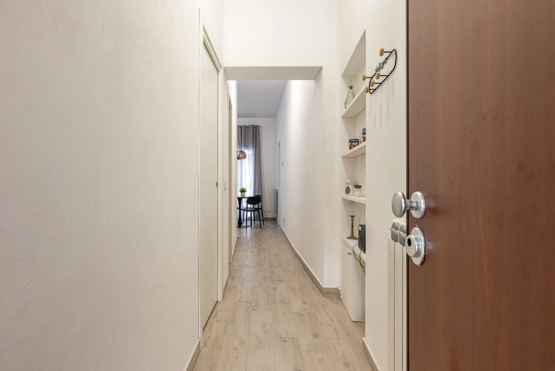 A narrow hallway with light wood flooring and built-in shelves.
