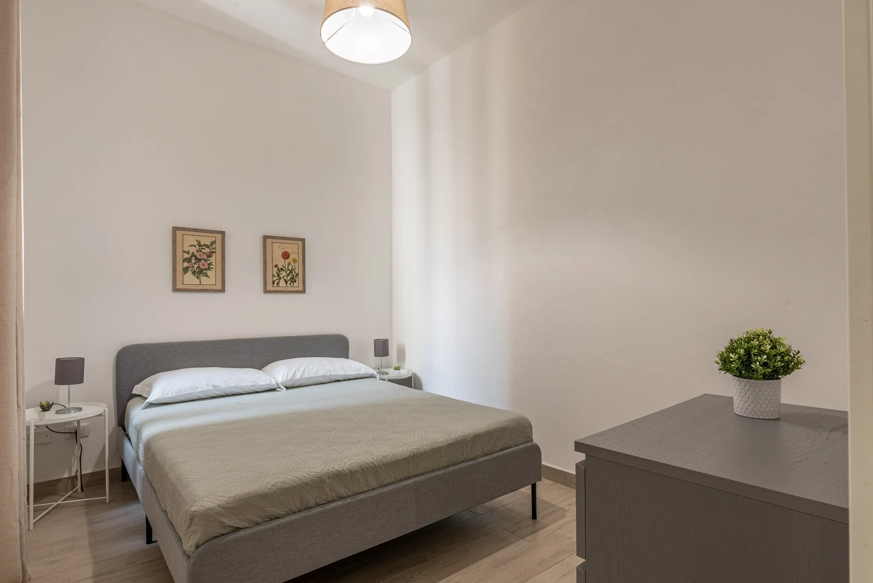 A bedroom with a bed, framed botanical prints, and a dresser.