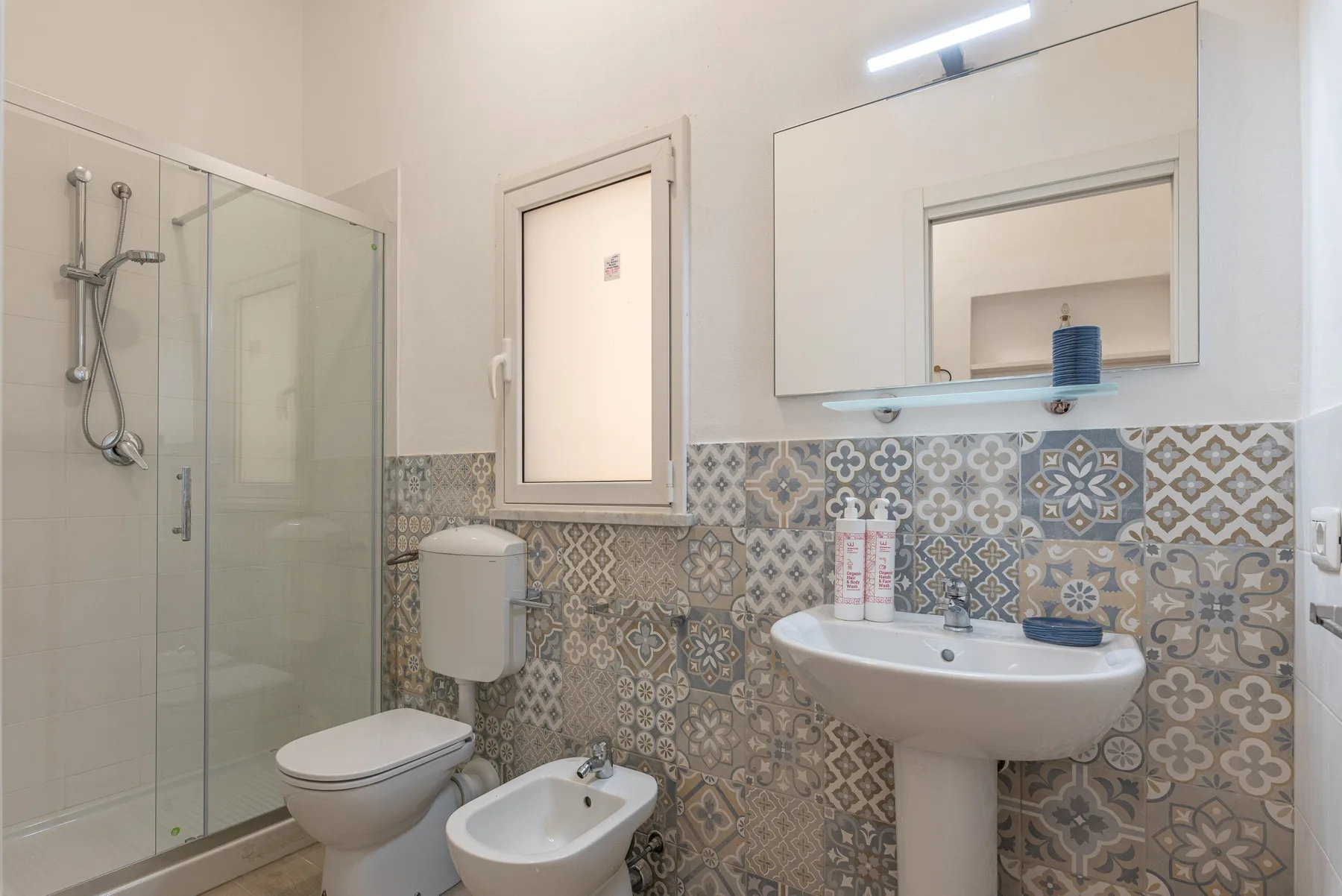 A tiled bathroom with a glass shower, toilet, bidet, and sink.