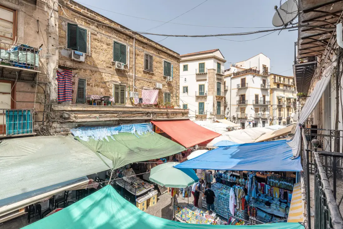 A busy outdoor market fills a narrow street beneath colorful awnings.
