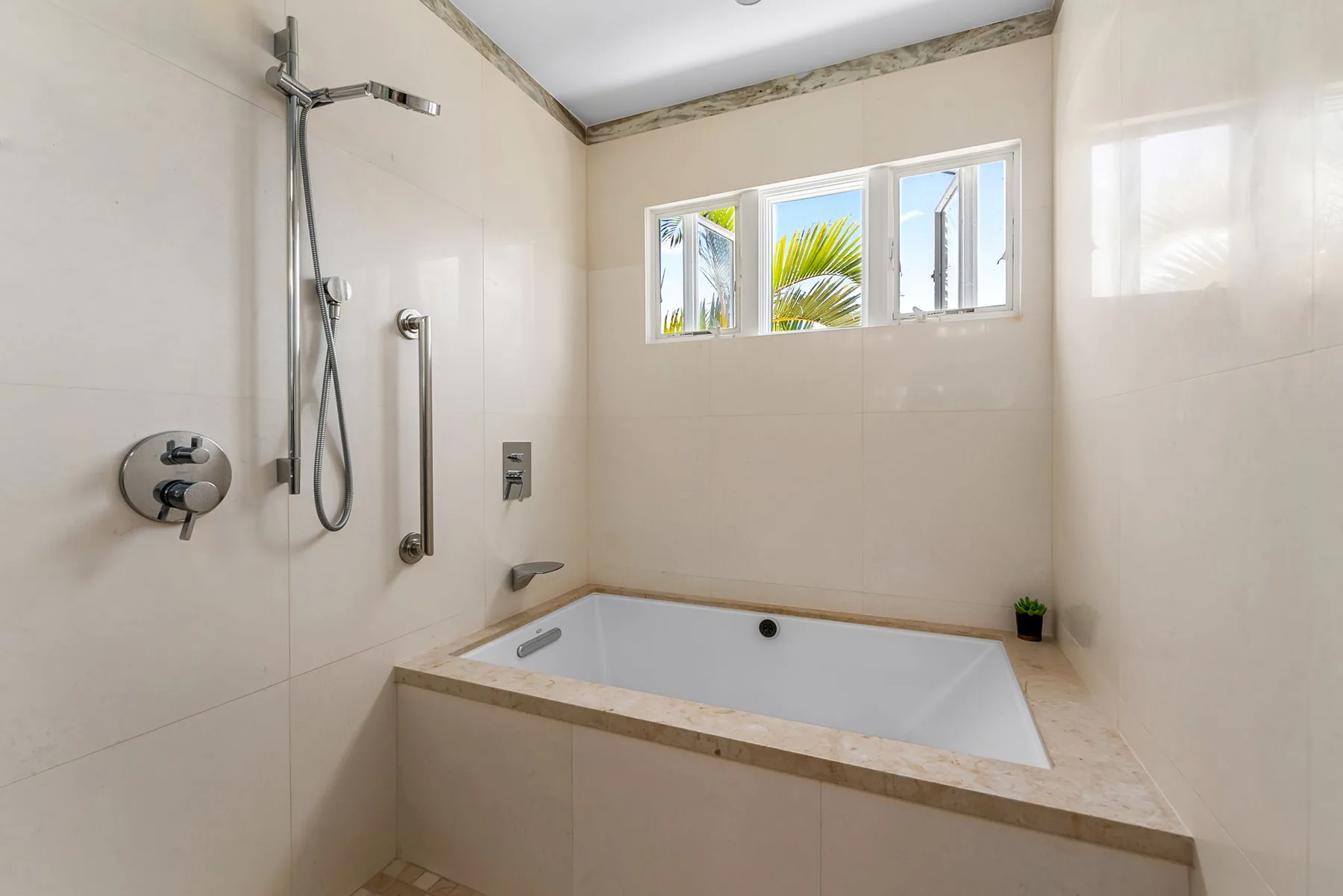 Un baño luminoso con una bañera empotrada bajo una fila de ventanas.