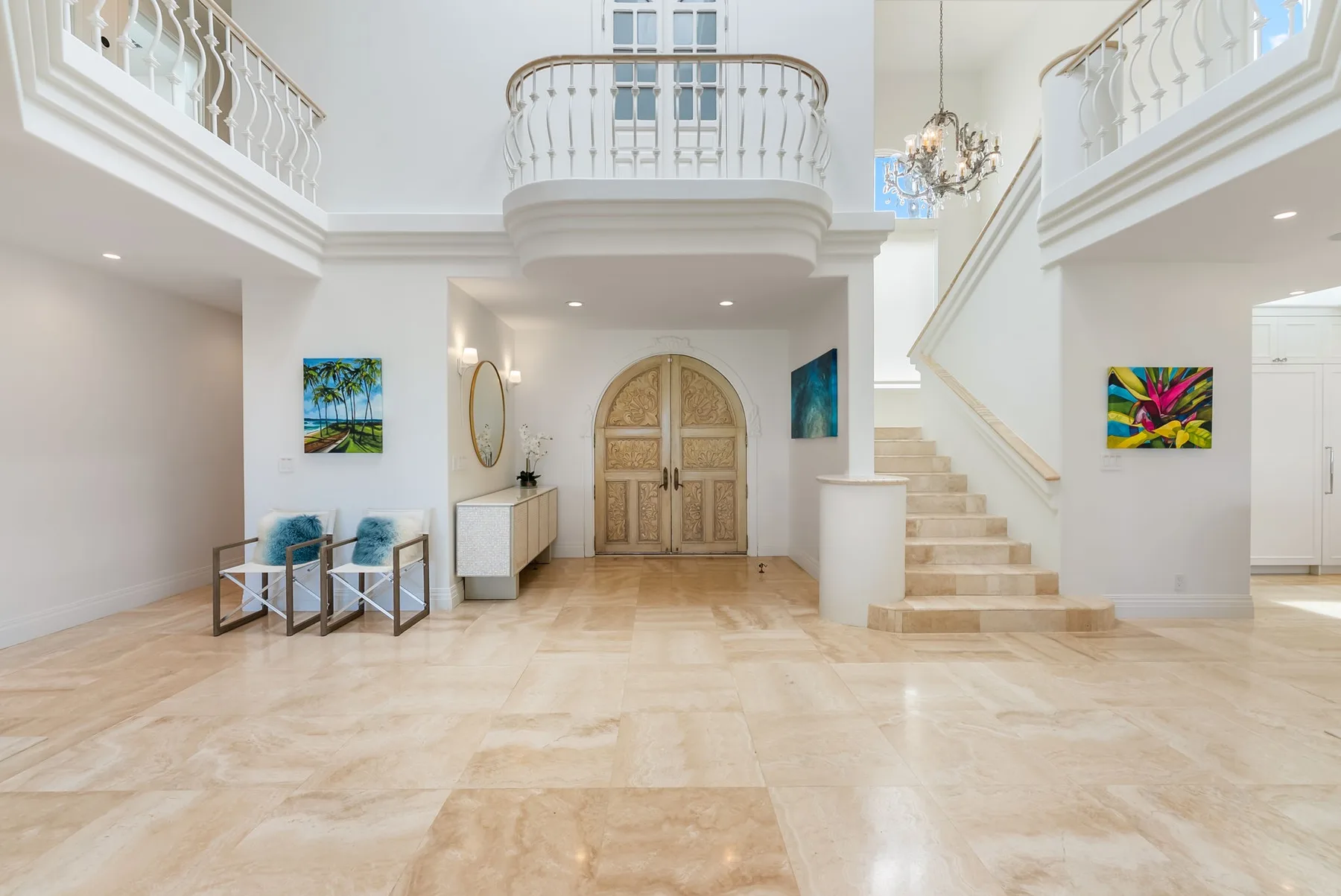 Un vestíbulo luminoso con un rellano superior curvo, una escalera y puertas dobles arqueadas.