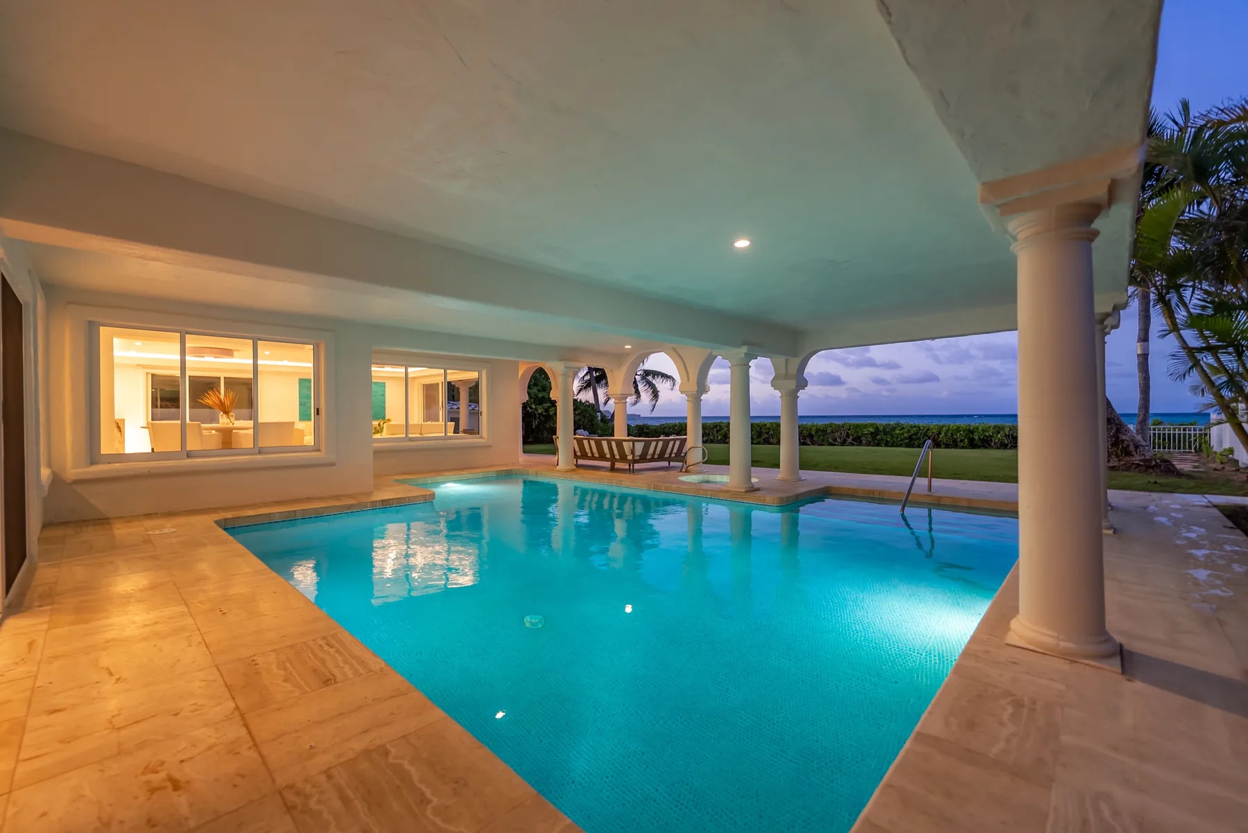 Una piscina exterior cubierta junto a un edificio, con palmeras y vistas al agua.