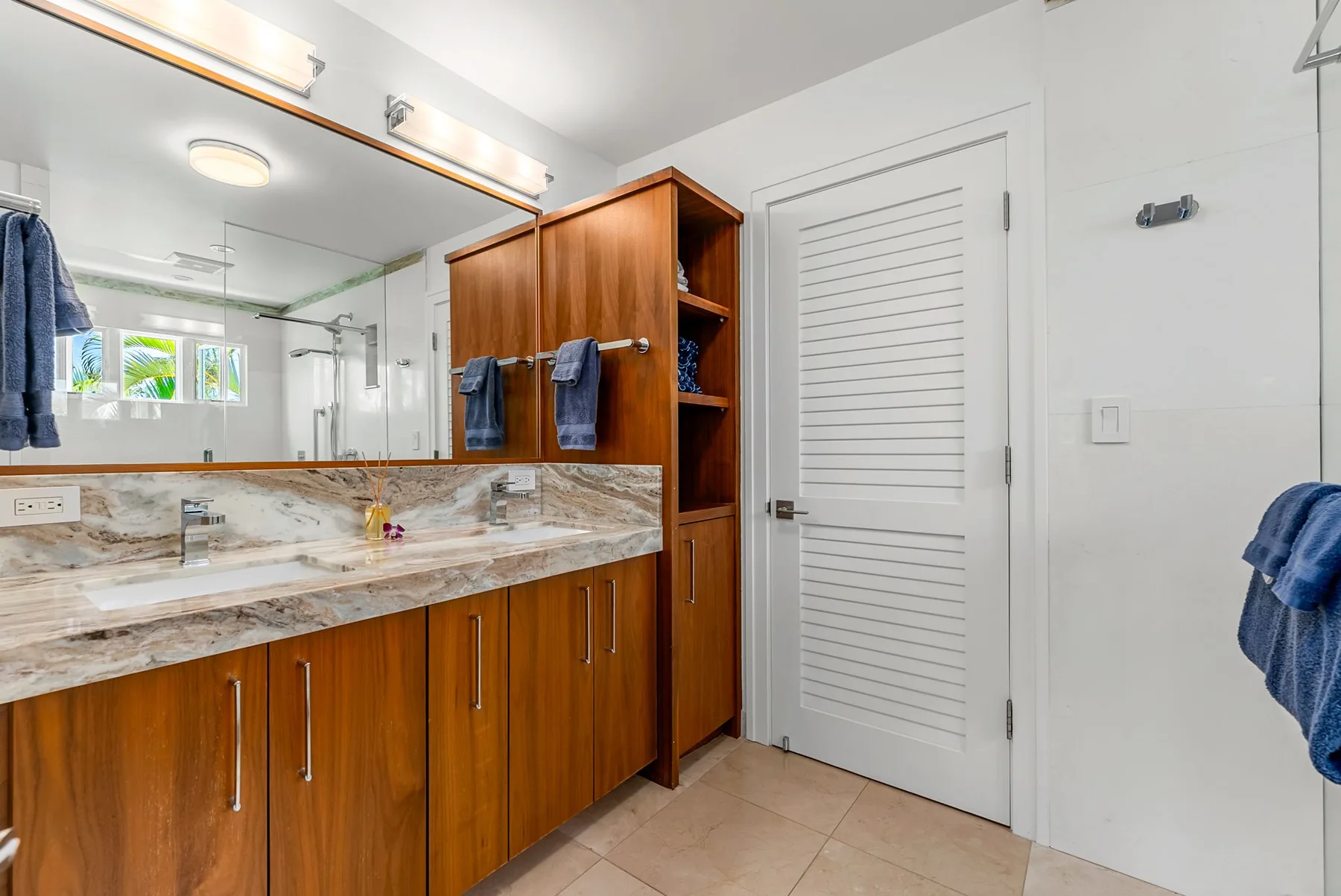 Un tocador de baño con un espejo amplio y una puerta blanca con rejillas.