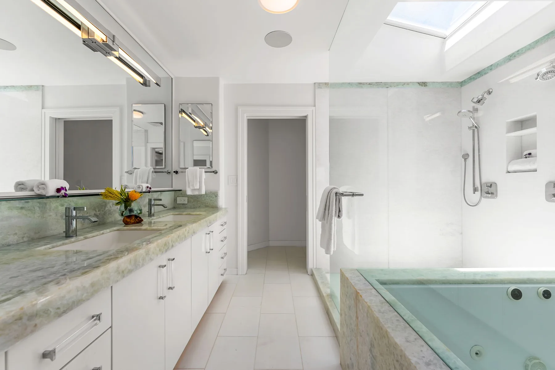 Un baño luminoso con un lavabo largo y una bañera con paneles de vidrio.